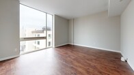 Located at 401 Granby St in the heart of Norfolk, VA, this two-bedroom, two-bathroom residence offers a well-designed single-floor layout with a clean, modern aesthetic. Rich, dark hardwood-style flooring runs throughout the entire unit, creating a warm and cohesive look from room to room. The open-concept living, dining, and kitchen area serves as the central hub of the home. The kitchen is outfitted with stainless steel appliances — including a refrigerator, electric range, and microwave — warm-toned wood cabinetry, gray countertops, a double-basin sink, and stylish pendant lighting that anchors the peninsula. Floor-to-ceiling windows in the living area flood the space with natural light and provide views of the surrounding Norfolk cityscape. Both bedrooms are generously proportioned with high ceilings, adding to the sense of openness. The primary bedroom features a large closet, while the second bedroom offers its own windowed wall for additional natural light. Four closets are distributed throughout, providing ample storage. The two bathrooms each feature white vanity cabinetry with gray countertops; one includes a shower-tub combination. A dedicated laundry area and utility room round out the functional layout of this well-appointed urban residence.