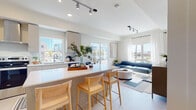 This thoughtfully designed single-floor residence offers a seamless blend of contemporary style and functional living. The open-concept layout connects the kitchen and living area, creating an inviting, light-filled space ideal for both daily living and entertaining. Large windows frame urban city views and flood the interiors with natural light, complemented by track lighting and clean white walls throughout.

The kitchen is a standout feature, equipped with stainless steel appliances including a refrigerator, range, microwave, and dishwasher. Sleek grey cabinetry pairs with white quartz countertops, while an integrated breakfast bar with seating provides a casual dining option. Light wood-tone flooring flows throughout the main living areas, adding warmth to the modern aesthetic.

The living room offers generous proportions, anchored by large windows with sheer white curtains that soften the incoming light and provide views of the surrounding cityscape. The bedroom is tranquil and well-lit, featuring a large window, light wood flooring, and ample space for furnishings. The full bathroom is finished with clean-lined white cabinetry, a white countertop vanity, and a full bathtub with shower combination. Overall, the space presents a cohesive, modern urban living environment with consistent finishes and an airy, open atmosphere.