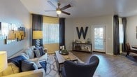 Located at 11875 W McDowell Rd in Avondale, Arizona, this single-story unit offers a thoughtfully designed layout with a cohesive, contemporary aesthetic. The living room serves as the central gathering space, featuring wood-look flooring, a ceiling fan with light fixture, and generous natural light from large windows dressed in vertical blinds and dark curtain panels. Two exterior doors provide convenient access points, and the open feel of the room accommodates both lounging and entertaining areas comfortably.

The kitchen is well-equipped with white cabinetry, dark countertops, and black appliances including a range, microwave, and dishwasher. A double-basin sink sits along a peninsula that opens toward the dining and living areas, promoting a connected, functional flow throughout the main living space.

The bedroom features plush carpeting, a ceiling fan, a mirrored sliding closet, and a large window that allows natural light to filter in. The room offers ample space for full bedroom furnishings and connects directly to the bathroom.

The bathroom includes wood-look flooring, a tub-shower combination with a white tile surround, a toilet, and a vanity with dark countertops. Recessed lighting and open shelving complete the space with a clean, organized appearance.