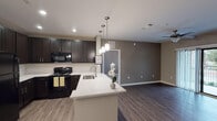 Located at 901 Hidden Valley Dr in Round Rock, Texas, this single-floor residence offers a well-designed layout with contemporary finishes throughout. The open-concept kitchen serves as a central hub, showcasing dark espresso cabinetry, a white subway tile backsplash, granite-look countertops, and a peninsula with pendant lighting overhead. Black appliances, including a refrigerator, range, and microwave, complement the kitchen's bold, modern aesthetic, while rich wood-look flooring ties the space together seamlessly into the adjoining living area. The living room features sliding glass doors opening to a private balcony, flooding the space with natural light and providing outdoor views. Ceiling fans are present throughout the bedrooms and living areas, enhancing comfort. The carpeted bedrooms are generously sized, each with windows that allow ample natural light and views of the surrounding area. The bathrooms are well-appointed, with one featuring a walk-in shower enclosed by a sliding glass door and finished with white subway tile, built-in shelving, and a mosaic tile floor. A second bathroom offers a soaking tub also surrounded by clean white subway tile. Dark vanities with granite countertops carry the home's consistent design language into the bathrooms, creating a cohesive and polished overall aesthetic.