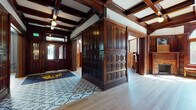 This remarkable space masterfully blends historic architectural grandeur with contemporary functionality. The entry foyer immediately establishes the building's character, featuring rich dark mahogany millwork, coffered ceilings with exposed wood beams, and a patterned geometric area rug atop light hardwood flooring. An elaborately carved wooden staircase serves as a central architectural showpiece, with ornate newel posts, turned balusters, and deep green carpeted treads leading to upper levels.

Throughout the space, dark wood wainscoting and decorative wall paneling are consistent hallmarks. Multiple rooms feature intricately detailed fireplace surrounds adorned with decorative tilework, adding warmth and historic character. A distinctive octagonal conference room showcases a coffered domed ceiling, a large round marble-topped table, arched windows, and a carved fireplace mantel. Additional meeting rooms feature bold decorative wallcoverings and generous natural light.

The fitness facility offers two well-equipped areas: one housing cardio equipment including treadmills and a stationary bike, and another dedicated to strength training with free weights, a mirrored wall framed by arched details, and natural stone accents. A billiards room and lounge area round out the amenity offerings, creating a sophisticated, multi-functional environment throughout.