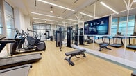 Located at 770 Juniper St NE in Atlanta's vibrant Midtown neighborhood, this well-appointed fitness center offers a comprehensive and thoughtfully designed workout environment across a single floor. The space is characterized by a clean, contemporary aesthetic, featuring light hardwood-style flooring, crisp white walls, and a bright linear lighting system that keeps the entire facility well-illuminated.

The main workout area is generously proportioned and houses an impressive selection of premium cardio equipment, including treadmills, elliptical trainers, and stair climbers, all arranged to maximize space and usability. A dedicated strength training zone features cable machines, a leg press, adjustable benches, and free weights, catering to a full range of training needs. Floor-to-ceiling mirrors amplify the sense of openness throughout the space, while a large mounted display screen adds a modern, connected feel to the main floor.

Distinctive black-framed glass partitions elegantly divide sections of the facility, creating defined zones while maintaining visual continuity. A built-in refreshment and amenity station with teal-accented shelving, a beverage cooler, and cubbies adds a thoughtful convenience. A separate enclosed room with its own glass door provides a more private area for additional equipment and focused training. The overall ambiance is professional, clean, and energizing.
