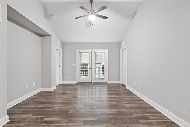 Bright and spacious living area with elegant wooden flooring, modern ceiling fan, and double doors leading to a balcony. - Grove Park Apartments