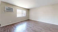 Located at 18415 Dearborn St in the Northridge neighborhood of Los Angeles, this one-bedroom, one-bathroom unit offers a practical and well-organized single-floor layout. The combined kitchen and living room serves as the heart of the home, featuring wood-style flooring and a ceiling fan that adds airflow and character to the space. The kitchen is appointed with white cabinetry, light countertops, a double-basin sink, stainless steel refrigerator, and a gas range, all set along a galley-style corridor with a window at the far end that brings in natural light. The living area is open and bright, with vertical blinds and a wall-mounted air conditioning unit providing comfort year-round. The bedroom is generously sized with plush carpeting, a wall-unit AC, and a dedicated closet with built-in shelving. Additional doors lead to the hallway and closet space, keeping the layout efficient. The bathroom features dark hardwood-style flooring, a vanity with an undermount sink, a large mirror, and clean white finishes throughout. Neutral tones across all rooms create a cohesive, move-in ready atmosphere well-suited for comfortable city living.