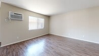 Located at 18415 Dearborn St in the Northridge neighborhood of Los Angeles, this one-bedroom, one-bathroom unit offers a practical and well-organized single-floor layout. The combined kitchen and living room serves as the heart of the home, featuring wood-style flooring and a ceiling fan that adds airflow and character to the space. The kitchen is appointed with white cabinetry, light countertops, a double-basin sink, stainless steel refrigerator, and a gas range, all set along a galley-style corridor with a window at the far end that brings in natural light. The living area is open and bright, with vertical blinds and a wall-mounted air conditioning unit providing comfort year-round. The bedroom is generously sized with plush carpeting, a wall-unit AC, and a dedicated closet with built-in shelving. Additional doors lead to the hallway and closet space, keeping the layout efficient. The bathroom features dark hardwood-style flooring, a vanity with an undermount sink, a large mirror, and clean white finishes throughout. Neutral tones across all rooms create a cohesive, move-in ready atmosphere well-suited for comfortable city living.