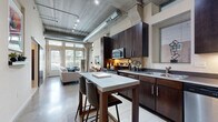 Located at 2838 Fremont Ave S in Minneapolis' vibrant Uptown neighborhood, this one-bedroom, one-bathroom loft delivers a striking industrial-chic aesthetic throughout its efficiently designed single-floor layout. The open-concept kitchen and living area serves as the heart of the space, showcasing soaring concrete ceilings with exposed silver ductwork and track lighting that lend an urban warehouse character. The well-appointed kitchen features rich dark wood cabinetry reaching nearly to the ceiling, stainless steel appliances including a range, microwave, dishwasher, and refrigerator, complemented by sleek countertops and a freestanding island with bar seating — ideal for casual dining and entertaining. Polished concrete floors flow through the main living area, where floor-to-ceiling windows and a glass door flood the space with abundant natural light and offer lush outdoor views. The bedroom provides a comfortable retreat with plush carpeting, generous window access, and three closets offering ample storage. The bathroom is clean and functional, featuring a tiled tub-shower combination, dark vanity cabinetry, and polished concrete flooring that ties back to the overall modern aesthetic. This loft combines bold architectural character with practical, well-considered design throughout.