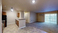 Located at 13660 W Sixth Ave in Airway Heights, Washington, this three-bedroom, two-bathroom residence offers a well-organized single-floor layout designed for comfortable everyday living. The open-concept kitchen and living area forms the heart of the home, featuring warm wood cabinetry, black appliances including a gas range, microwave, and refrigerator, and a peninsula with a built-in sink that provides a natural transition between the kitchen and the carpeted living room. The living room is generously sized, equipped with a wall-mounted HVAC unit, and opens directly to a private balcony through sliding glass doors fitted with vertical blinds, allowing for natural light and outdoor views. The primary bedroom is a spacious retreat with two windows, plush carpeting, and its own HVAC unit. The two additional bedrooms are well-proportioned, each finished with neutral-toned walls and soft carpet. Both bathrooms are functionally appointed — one features a vanity with wood cabinetry and a walk-in shower, while the other includes a full soaking tub and shower combination. Stone-look tile flooring runs through the kitchen and bathrooms, complementing the warm, neutral palette carried throughout the entire residence.