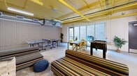 Located in Eagan, MN, this single-floor amenity space spans a generous footprint and is divided into two distinct functional zones connected by a corridor. A bold design aesthetic ties the space together, with yellow-painted exposed ceilings, ductwork, and piping creating an energetic industrial character throughout.

The game and lounge area serves as the social hub of the space. It features striped upholstered seating, knit poufs, and a round coffee table arranged around a wall-mounted flat-screen TV. A large wooden game table with open shelving stocked with board games anchors the room, while a foosball table and two ping-pong tables provide ample entertainment options. Large floor-to-ceiling windows allow natural light to pour in, and a dining table with chairs offers a casual gathering spot. Pendant lighting adds warmth to the atmosphere.

The dedicated bike storage area is expansive and highly organized, featuring multiple vertical and horizontal bike racks capable of accommodating a large number of bicycles. Secure individual storage lockers line the walls, providing private storage options. A bike wash station with a hose is also present, making maintenance convenient. The polished concrete floors and bright linear lighting ensure the area remains clean and functional. This well-appointed space reflects a strong commitment to active, community-oriented amenities.