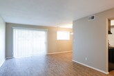 This single-floor residence offers a well-organized layout designed for comfortable everyday living. The open living and dining area is finished with warm wood-look flooring that extends throughout the main spaces, complemented by neutral-toned walls and clean white trim. Large vertical blinds cover a sliding glass door that invites natural light into the living area, while a modest pendant light fixture marks the adjacent dining space. The kitchen is equipped with a black electric range, an overhead exhaust hood, granite-look countertops, and a subway tile backsplash, with light cabinetry adding a contemporary touch. A dedicated pantry or utility closet provides additional storage just off the kitchen. The bedrooms are carpeted and feature neutral walls with windows fitted with horizontal blinds. The primary bedroom is particularly functional, offering access to a walk-in closet and a secondary door leading to a hallway or additional space. A second bedroom provides a quiet, well-lit retreat. The full bathroom includes a granite-topped vanity with gray cabinetry, a large mirror, wood-look flooring, and a tiled shower-tub combination. Textured ceilings are present throughout, and the overall aesthetic is clean, neutral, and move-in ready.