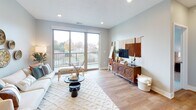 This thoughtfully designed single-floor residence blends contemporary style with functional living. The open-concept layout connects the kitchen, dining, and living areas into one cohesive space. The kitchen is outfitted with stainless steel appliances, a two-tone cabinet design featuring crisp white uppers and warm taupe lowers, quartz countertops, and a central island with pendant lighting — ideal for both meal prep and casual dining. Recessed lighting and light wood-style flooring carry throughout the main living area, adding warmth and brightness.

The living room is generously proportioned, anchored by large sliding glass doors that flood the space with natural light and open directly onto a private balcony overlooking a lush outdoor landscape. The balcony provides a comfortable retreat with pleasant views of the surrounding greenery.

The bedrooms offer a calm, restful atmosphere with plush carpeting, ceiling fans, and ample natural light from large windows. The primary bedroom provides a serene escape with soft neutral tones and generous space. The bathroom features hardwood-style flooring, a clean white vanity with dark wood cabinetry, and a shower-tub combination. Throughout, the soft gray color palette and modern finishes create a cohesive, welcoming aesthetic.