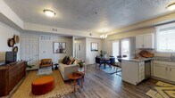 This single-floor unit in Tooele, Utah offers a thoughtfully designed open-concept layout where the living, dining, and kitchen areas flow seamlessly together. The living room features wood-style flooring, a textured ceiling, and a tray ceiling accent, creating a warm and inviting atmosphere. Large windows and a sliding glass door in the dining area allow natural light to fill the space while providing outdoor views, complemented by a elegant chandelier overhead.

The kitchen is well-equipped with stainless steel appliances, including a refrigerator, electric range, and microwave. White shaker-style cabinetry pairs with granite countertops, and a peninsula provides additional workspace and a casual dining option. A window above the sink brings in additional natural light.

The bedroom is carpeted for comfort and features a generously sized window with blinds, a closet, and ample space for furnishings. The bathroom continues the granite countertop theme with white cabinetry, a large mirror, wood-style flooring, and a shower-tub combination. Throughout the unit, neutral gray walls create a versatile backdrop, and consistent finishes tie the space together cohesively.