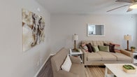 Located at 1445 16th St N in Saint Petersburg, Florida, this single-floor residence offers a thoughtfully designed layout with a warm, neutral aesthetic throughout. The living area serves as the heart of the home, featuring wood-look flooring, soft neutral walls, and comfortable seating accented by colorful throw pillows. A framed mirror and bold elephant wall art add character to the space, while a ceiling fan overhead ensures year-round comfort. Adjacent to the living area, a compact dining space provides a functional area for meals. The kitchen is efficiently organized with crisp white cabinetry, granite-look countertops, stainless steel appliances including a range and over-the-range microwave, and a double-basin sink beneath a window that allows natural light to fill the space. Recessed lighting further brightens the kitchen. The bedroom is a restful retreat, outfitted with wood-look flooring, a ceiling fan with light fixture, and a window dressed with drapes that offer both privacy and natural light. The bathroom features a tub-shower combination clad in classic white subway tile, accented by a decorative mosaic border strip and brushed nickel fixtures, lending a clean and timeless finish to the space.
