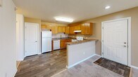 Located at Friendship Village in Harrington, Delaware, this one-bedroom, one-bathroom residence offers a well-organized single-floor layout designed for comfortable everyday living. The open-concept kitchen and living room area serves as the heart of the home, featuring warm honey-toned oak cabinetry, laminate countertops, and white appliances including a range, dishwasher, and refrigerator. A peninsula counter provides a natural transition between the kitchen and the carpeted living area, which benefits from a sliding glass door fitted with vertical blinds that allows an abundance of natural light to fill the space. The living area is generously proportioned, offering ample room for a variety of furniture arrangements. The spacious primary bedroom is finished with plush carpet and features a large window that brings in natural light and views of the surrounding community. A dedicated closet provides convenient storage. The full bathroom is cleanly appointed with a single-sink vanity with a light stone-style countertop, oak cabinetry, a tub/shower combination, and wood-look flooring. A hallway connects the main living spaces, completing this practical and cohesive floor plan.