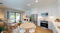 Located in Bonita Springs, FL, this two-story home offers a thoughtfully designed layout across two well-proportioned floors. The main level features an open-concept living, dining, and kitchen area filled with natural light, anchored by warm wood-look flooring that flows seamlessly throughout. The kitchen is equipped with stainless steel appliances, crisp white cabinetry, a subway tile backsplash, and clean countertops, complemented by an adjacent dining area with a round natural wood table. The living room offers a relaxed coastal ambiance with a neutral palette, tasteful wall art, and lush indoor greenery. A hallway on this level, accented by a vibrant beach-themed mural, leads to a full bathroom and laundry area. Two outdoor patio spaces extend the living area, one featuring a covered pergola with pavers, turf, and tropical plantings for a private Florida retreat. Upstairs, the spacious primary bedroom is a serene escape with a large window offering treetop views, warm wood flooring, and ample closet space. A second full bathroom serves the upper level. Modern hardware, recessed lighting, and a clean, contemporary aesthetic are consistent throughout, creating a cohesive and comfortable living environment.