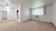 Located at 72 S Fremont Ave in Bellevue, PA, this single-floor residence offers a straightforward and functional layout across two bedrooms, one bathroom, and a kitchen. The living area features neutral wall-to-wall carpeting, white walls, and a tiled ceiling, creating a clean and understated ambiance. A wall-unit air conditioner and bright vertical blinds accent the main living space, which receives natural light through a prominently placed window. The spacious primary bedroom is generously sized, with soft carpeting, a baseboard heating unit, and a window framing an outdoor view of green surroundings. It also features a set of wide louvered bi-fold closet doors, providing ample storage. The second bedroom offers a similarly simple layout with carpeting, a baseboard heater, and its own window. The kitchen is compact yet well-equipped, featuring warm wood cabinetry, white appliances including a refrigerator, dishwasher, and range, along with light tile flooring and a window for ventilation. The bathroom is finished with white tile flooring, peach-toned wall tile accents, a tub-shower combination, a white vanity with brass fixtures, and a mirrored medicine cabinet. A classic wood-paneled entry door with brass hardware completes the welcoming interior character of this practical home.