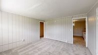 Located at 3 Carleton Rd in Storrs Mansfield, Connecticut, this single-floor, three-bedroom, one-bathroom home offers a compact and functional layout. Throughout the space, a consistent design theme is established by vertical tongue-and-groove style wall paneling in a neutral gray tone, complemented by white trim and crown molding in select rooms.

The bedrooms are carpeted and served by baseboard heating units, ensuring warmth throughout the seasons. The spacious primary bedroom features an open layout with ample room for furnishings, while the two additional bedrooms each include built-in closets with wooden hanging rods. One of the secondary bedrooms benefits from a window that allows natural light to filter in.

The full bathroom is finished with tile flooring, white vertical paneling, a vanity with cabinet storage, a bathtub, and a window that provides ventilation and natural light. A dedicated laundry area and a hallway connect the rooms efficiently. The kitchen area features tile flooring and includes space for a full-size refrigerator.

A front entry area with windows and access to the exterior completes the layout, offering a welcoming transition into the home. Overall, the space presents a straightforward, utilitarian character well-suited for practical, everyday living.