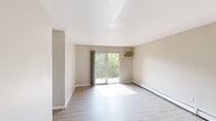 Located at 700 Riddle Rd in Cincinnati, Ohio, this single-floor unit offers a clean, functional layout with updated finishes throughout. The living area is bright and open, featuring light wood-tone luxury vinyl plank flooring, neutral wall tones, and a sliding glass door that leads to a private balcony overlooking a lush, tree-lined backdrop. A wall-mounted air conditioning unit and baseboard heating provide year-round climate control. The kitchen is well-appointed with granite-style countertops, white cabinetry, a mosaic tile backsplash in soft gray tones, a stainless steel sink, and a freestanding electric range. The bedroom area offers ample storage with built-in open shelving units on either side of the room, complemented by a closet with a paneled door. A horizontal window in the bedroom frames tranquil views of the surrounding greenery. The bathroom is clean and straightforward, featuring a full-size soaking tub with white tile surround, a white vanity, and vinyl plank flooring that complements the rest of the unit. Throughout the space, the consistent neutral palette and natural light create a calm, welcoming atmosphere suitable for everyday living.
