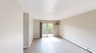 Located at 700 Riddle Rd in Cincinnati, Ohio, this single-floor unit offers a clean, functional layout with updated finishes throughout. The living area is bright and open, featuring light wood-tone luxury vinyl plank flooring, neutral wall tones, and a sliding glass door that leads to a private balcony overlooking a lush, tree-lined backdrop. A wall-mounted air conditioning unit and baseboard heating provide year-round climate control. The kitchen is well-appointed with granite-style countertops, white cabinetry, a mosaic tile backsplash in soft gray tones, a stainless steel sink, and a freestanding electric range. The bedroom area offers ample storage with built-in open shelving units on either side of the room, complemented by a closet with a paneled door. A horizontal window in the bedroom frames tranquil views of the surrounding greenery. The bathroom is clean and straightforward, featuring a full-size soaking tub with white tile surround, a white vanity, and vinyl plank flooring that complements the rest of the unit. Throughout the space, the consistent neutral palette and natural light create a calm, welcoming atmosphere suitable for everyday living.