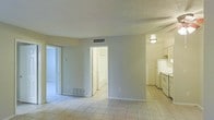 This single-floor residence offers a straightforward and functional layout designed for comfortable everyday living. The main living area is finished with light-toned ceramic tile flooring that extends throughout the space, contributing to a clean and cohesive aesthetic. Neutral-colored walls and a textured ceiling complement the understated design, while flush-mounted ceiling lighting provides consistent illumination. Ventilation is well-managed with visible HVAC vents in both the ceiling and floor, supporting year-round climate control. An open passageway connects the living area directly to the kitchen, which is equipped with white appliances including a range and refrigerator, alongside light-colored cabinetry and an overhead range hood. Interior doorways lead to additional rooms, including what appears to be a bedroom with a closet, suggesting a practical floor plan that maximizes the use of available space. The overall ambiance is bright and neutral, offering a blank canvas well-suited for personalization. The single-story layout ensures easy accessibility throughout, making it a practical and livable space from end to end.