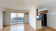 This single-floor unit is characterized by clean, neutral finishes and a practical layout that maximizes functionality throughout. The open living area features light hardwood flooring that extends seamlessly across the space, complemented by crisp white walls and a ceiling fan. Sliding glass doors lead to a private balcony enclosed by a latticed railing, allowing natural light to fill the room. A wall-mounted air conditioning unit provides climate control.

The semi-open kitchen is separated from the living area by a partial wall and peninsula counter with granite-style countertops. Rich wood cabinetry lines both walls from floor to ceiling, offering ample storage. Stainless steel appliances include a full-size refrigerator, gas range, and built-in microwave, while tile flooring and a window above the sink add practicality and light.

The bedrooms feature the same hardwood flooring and ceiling fans, with one room offering a wide window that invites outdoor views and abundant natural light. Both rooms include open closets for convenient storage.

The bathroom is finished with tile flooring, a tub and shower combination enclosed by sliding glass doors, a vanity with a single-basin sink, and a small window for ventilation.