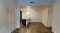 This single-floor space offers a clean, open-concept design that seamlessly connects the kitchen and living areas. The kitchen is anchored by a peninsula with a light-toned countertop and an undermount sink, complemented by dark cabinetry that adds contrast to the bright white walls. A decorative pendant light hangs above the peninsula, providing focused task lighting and an understated modern touch. Adjacent to the kitchen, the living area is finished with rich, dark hardwood-style flooring that runs throughout the main space, lending warmth and continuity to the interior. A ceiling fan with a brushed metal finish occupies the center of the living area, offering both practical ventilation and a subtle design element. Recessed lighting and a visible HVAC vent in the ceiling ensure comfortable climate control. The walls are painted in a crisp, neutral white, creating a bright and airy atmosphere that makes the space feel open and inviting. Full-height interior doors and clean baseboards reflect a well-maintained, move-in-ready condition. The overall ambiance is modern and functional, with a cohesive design palette that balances dark and light elements throughout.