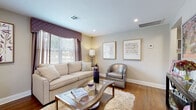 Located at 1 Marion Pepe Dr in Lodi, New Jersey, this single-floor residence offers a cohesive and elegantly styled living environment. The living room serves as the centerpiece of the home, featuring warm hardwood flooring, recessed lighting, and a large bay window dressed with decorative valances and blinds that allow natural light to fill the space. A plush sofa, silver accent chair, and a glass-top coffee table contribute to the room's refined, contemporary aesthetic, complemented by framed artwork on neutral-toned walls.

The kitchenette is compact yet functional, outfitted with rich dark cabinetry, a stainless steel refrigerator, light tile flooring, and a tiled backsplash. A small bistro-style dining set nestled beside a window provides a bright and cozy spot for casual meals.

The primary bedroom offers a tranquil retreat with hardwood floors, sheer curtains that filter soft natural light, decorative valances, and warm, coordinated bedding. A second bedroom, finished with hardwood floors and a window with a stylish valance, provides flexible use as a guest room or additional sleeping space.

The bathroom is clean and well-finished, featuring tiled walls with accent border detailing, tile flooring, and a combination tub and shower, creating a practical and polished space. Throughout, the residence maintains a warm, neutral color palette with carefully chosen accents.