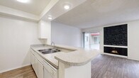 Located at 444 S Kingsley Dr in the Koreatown neighborhood of Los Angeles, this efficiently designed single-floor unit makes the most of its compact footprint. The open-concept kitchen and living area form the heart of the space, featuring warm wood-look flooring that runs throughout. The kitchen is outfitted with white cabinetry, granite-style countertops, a double-basin sink, and a white electric range. A peninsula counter extends into the living area, creating a natural divide between cooking and lounging spaces while maintaining an open, airy feel. Recessed lighting with a tray ceiling detail above the kitchen adds architectural interest.

The living area is bright and welcoming, highlighted by a dramatic floor-to-ceiling black stone fireplace that serves as a striking focal point. Sliding glass doors flood the room with natural light and provide outdoor access, while an additional window contributes to the sun-filled ambiance. A textured ceiling adds subtle character throughout.

A hallway connects to a well-appointed bathroom featuring wood-look flooring, a wide granite-style vanity with under-sink storage, a large wall mirror, and a tub-shower combination with sliding glass doors. A dedicated closet and entryway hallway complete the layout, offering practical storage within a streamlined, functional floor plan.