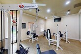 Located in Huffman, TX, this dedicated fitness center offers a well-equipped exercise space designed to support a comprehensive workout routine. The room is finished with warm, neutral-toned walls, crown molding, and carpeted flooring, creating a clean and inviting atmosphere for physical activity.

The space is outfitted with several Quantum-brand strength training machines, including cable pulley systems, a lat pulldown station, a leg press, and a seated exercise machine, providing users with a variety of resistance training options. A stationary recumbent bike adds a cardio element to the facility. A full-length wall mirror on one side of the room enhances the sense of space and allows users to monitor their form during workouts.

Natural light enters through a large glass-panel exterior door and a window fitted with blinds, both offering views of the surrounding green outdoor area. Recessed lighting and a ceiling fan with built-in light fixture ensure the space remains well-lit and comfortable. Two wall-mounted flat-screen televisions provide entertainment during workouts. A posted fitness room rules sign reflects the managed, community-oriented nature of the facility. The combination of functional equipment, thoughtful finishes, and practical amenities makes this fitness center a convenient and effective exercise destination.