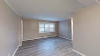 Located at 26 Bishop Ln in Groton, Connecticut, this single-floor unit offers a clean, updated interior with a cohesive neutral color palette and consistent trim work throughout. The living area is generously sized, featuring light gray luxury vinyl plank flooring, crown molding, and a large window that allows natural light to fill the room. Baseboard heating units are present throughout the space, ensuring efficient warmth during New England winters. A separate bedroom is carpeted and similarly appointed with crown molding, a window with blinds, and baseboard heating, providing a comfortable and quiet retreat. The kitchen is outfitted with white cabinetry, light marble-style countertops, stainless steel appliances including an electric range, and matching vinyl plank flooring that ties seamlessly into the adjacent living areas. A dedicated entry area connects the front door directly to the living and kitchen spaces, offering a practical and open flow. The full bathroom is finished in a crisp white palette, complete with a soaking tub and shower combination, a white vanity, vinyl plank flooring, and a frosted window for privacy and ventilation. Overall, the unit presents a well-maintained, move-in-ready interior with modern updates and functional design throughout.