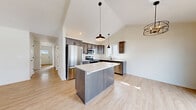 Located at 3355 Union St in North Chili, NY, this two-story home offers a well-designed layout across two floors and a basement. The main level opens with a clean, bright entryway featuring a paneled door with transom window and light hardwood flooring that continues throughout the common areas. The open-concept kitchen is a standout, boasting soaring vaulted ceilings, dark cabinetry with modern hardware, stainless steel appliances, a large center island with a white quartz countertop, and pendant lighting. The adjacent living area shares the vaulted ceiling and benefits from natural light through multiple windows, with a ceiling fan adding to the comfort. The upper floor houses all three bedrooms, including a generously sized primary suite with its own walk-in closet fitted with wire shelving. The two bathrooms are finished with light hardwood-style flooring, dark hardware, and clean white fixtures. Bedrooms feature plush carpeting and neutral tones throughout. An unfinished basement provides additional utility space with a water heater and structural support columns. A two-car garage with drywalled walls completes the home, offering ample storage and parking.
