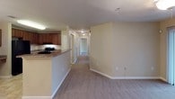 This single-floor residence offers a well-organized layout across two bedrooms and two bathrooms, designed with practicality and comfort in mind. The entryway welcomes residents through a paneled front door, transitioning from tile flooring into carpeted living areas finished in warm, neutral tones throughout.

The kitchen is equipped with rich medium-toned wood cabinetry, granite-style countertops, and black appliances including a refrigerator and electric range. A raised breakfast bar connects the kitchen to the adjacent living and dining area, creating an open, communicative flow. The main living space is carpeted and opens down a hallway leading to both bedrooms and bathrooms.

The bedrooms are carpeted, with neutral walls and white trim. The primary bedroom features a ceiling fan with lighting and a window overlooking greenery, adding natural light to the space. The second bedroom is similarly sized with the same neutral palette.

Both bathrooms feature tile flooring in a warm stone pattern, dark wood vanities, and white fixtures. One bathroom includes a shower-tub combination with a curved curtain rod, while the second offers a walk-in style shower-tub unit. Overhead ventilation is present in each bathroom, contributing to a clean, functional design throughout.