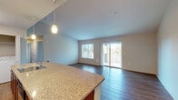 This single-floor residence offers a well-designed open-concept layout that seamlessly connects the kitchen and living area. The kitchen is outfitted with warm-toned wood cabinetry, granite countertops, stainless steel appliances including an electric range, microwave, refrigerator, and dishwasher, and is anchored by a curved peninsula with a built-in sink and pendant lighting overhead. Light wood-tone flooring runs throughout the kitchen and extends into the living area.

The living room is generously proportioned, featuring vaulted ceilings that enhance the sense of openness. Large windows and a sliding glass door flood the space with natural light and provide direct access to a private balcony with outdoor views of surrounding greenery. Wood-style flooring continues throughout this area, adding a cohesive, modern aesthetic.

The bedroom is carpeted for comfort and includes a large window with nature views, as well as access to a spacious walk-in closet with wire shelving along multiple walls. The full bathroom features a granite-topped vanity with wood cabinetry, a tub-shower combination with a mirrored surround, and wood-style flooring.

A convenient in-unit laundry area with a full-size washer and dryer rounds out the practical amenities of this thoughtfully arranged residence.