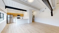 Located at 21 Erie Blvd in Albany, NY, this 2-bedroom, 1-bathroom unit blends industrial character with modern finishes throughout. The open-concept kitchen and living area forms the heart of the space, where exposed black steel beams and white-painted shiplap ceilings create a striking loft-inspired aesthetic. Light hardwood flooring flows seamlessly throughout, enhancing the bright, airy atmosphere. The kitchen is well-appointed with warm wood upper cabinetry, white lower cabinets, stainless steel appliances including a refrigerator, range, and microwave, and a peninsula that provides additional prep and dining space. Large industrial-style windows invite abundant natural light and frame outdoor views. The spacious primary bedroom features a bold black sliding closet door and exposed beam detailing, while the second bedroom offers a transom-style window that adds a unique architectural touch. Three closets provide ample storage throughout the unit. The full bathroom is finished with dark hexagonal tile flooring, a white vanity with matte black fixtures, a framed mirror, and a full tub-shower combination. A dedicated laundry area and in-unit hallway round out this well-designed, character-rich home.