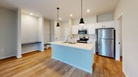This single-floor unit at S Burnsfield Ave in Sioux Falls, South Dakota, offers a thoughtfully designed layout with a clean, contemporary aesthetic throughout. The open-concept living and kitchen area serves as the heart of the space, featuring warm-toned luxury vinyl plank flooring that flows seamlessly between rooms. The kitchen is equipped with stainless steel appliances, including a refrigerator, electric range, and built-in microwave, complemented by white cabinetry, light quartz countertops, and a central island with a built-in sink and pendant lighting overhead. A dedicated drop zone with a built-in bench adds functional convenience near the entry.

The bedrooms feature plush carpeting and windows that bring in natural light, with exposed ductwork adding an industrial touch. Two bathrooms serve the unit, one featuring a walk-in shower and the other a soaking tub, both finished with wood-look flooring, white vanities, and striking dark marble-style countertops with matte black hardware accents.

A dedicated laundry area houses a full-size top-loading washer and dryer alongside wire shelving for additional storage. Neutral wall tones and consistent finishes throughout create a cohesive, move-in-ready atmosphere.