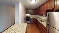 This 2-bedroom, 1.5-bathroom residence spans a generous single floor, offering a well-organized layout with comfortable living spaces throughout. Rich hardwood-style flooring flows consistently across the main living areas, dining space, and bedrooms, creating a warm and cohesive aesthetic.

The kitchen is a standout feature, outfitted with rich dark wood cabinetry extending to the ceiling for abundant storage, granite-look countertops, and a full suite of stainless steel appliances including a refrigerator, dishwasher, and range. A pass-through countertop connects the kitchen to the main living area, enhancing the open feel of the space.

The living room is bright and spacious, featuring multiple windows with outdoor views and a convenient wall-unit air conditioner alongside baseboard heating. A separate dining area is accented by a ceiling light fixture and an exterior door that brings in additional natural light.

Both bedrooms are generously sized, with the primary bedroom showcasing dual louvered bi-fold closet doors offering ample storage. The full bathroom includes a tub/shower combination with tile surround, a pedestal sink, and a large mirror with overhead lighting. The half bathroom features a wood medicine cabinet and a towel bar, providing practical convenience.