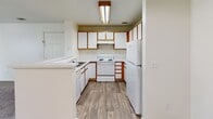 Located at 744 Mockingbird St in Brighton, Colorado, this single-floor home offers a straightforward and functional layout designed for comfortable everyday living. The kitchen is well-equipped with ample wood-trimmed white cabinetry, a full suite of white appliances including an electric range and refrigerator, a built-in dishwasher, and a peninsula that opens toward the adjoining dining and living areas. Wood-look plank flooring runs throughout the kitchen and extends into the entry and dining space, while a pendant light fixture adds a warm accent above. The open living area is generously sized, filled with natural light from a large front-facing window, and features neutral carpet that carries through to the bedrooms. The primary bedroom is spacious and bright, offering dual closets with bifold doors and built-in shelving rods for ample storage. Additional bedrooms are finished with the same neutral carpet and clean white walls. The bathroom features wood-look tile flooring, a vanity with a speckled countertop, and a tiled shower/tub combination with a grab bar and towel bar. Throughout the home, a clean, neutral palette and an abundance of natural light create a bright and open atmosphere.