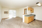 This single-floor unit offers a practical and well-organized layout designed for comfortable daily living. The kitchen is efficiently arranged with light oak cabinetry spanning both upper and lower sections, providing ample storage space. It is equipped with a coil-burner electric range, built-in microwave, dishwasher, and a full-size refrigerator, all complemented by grey laminate countertops. The kitchen opens toward the living area, which features neutral carpet flooring and a bright, open feel enhanced by a sliding glass door that leads to an outdoor view, allowing natural light to fill the space. The living area is generously sized, with clean white walls, carpet flooring, and straightforward access to the entryway. The bedroom is carpeted and features a ceiling fan with light fixture, a standard window with blinds for natural light and privacy, and baseboard heating. The bathroom includes a full-size soaking tub with shower surround, a wood-cabinet vanity with grey countertop and integrated sink, a large mirror with overhead lighting, and tile flooring. Consistent design elements — including oak-toned cabinetry, grey countertops, and neutral tones throughout — give the unit a cohesive and functional aesthetic well-suited to everyday living.