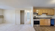 Located at 479 S Broadway in Lawrence, MA, this 2-bedroom, 1-bathroom unit offers a practical and well-organized single-floor layout. The living area features light-colored carpeting and a textured ceiling, providing a clean and neutral backdrop throughout. An open-concept flow connects the living space to the kitchen, which is equipped with warm honey-toned wood cabinetry, dark laminate countertops, a stainless steel gas range with overhead exhaust, a black dishwasher, a black refrigerator, and a double-basin sink — all set atop wood-look flooring. A hallway leads to both bedrooms and the bathroom, offering a clear separation between living and sleeping areas. The primary bedroom is a comfortable size, featuring carpet flooring, a double-door closet with built-in shelving, a baseboard heating unit, and a window with outdoor views. The second bedroom is similarly carpeted with its own closet and window. Baseboard heating and a wall-unit air conditioner provide year-round climate control. The full bathroom includes tile flooring, a tub/shower combination, a toilet, and a wood-vanity with countertop. Textured ceilings are consistent throughout the unit.