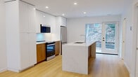 This contemporary three-floor townhouse at 6070 Almon Street in Halifax offers a thoughtfully designed layout across two bedrooms, four bathrooms, and multiple living areas. Light hardwood flooring runs throughout each level, complemented by crisp white walls and recessed lighting that create a clean, modern aesthetic.

The main floor features an open-concept kitchen with striking two-tone cabinetry — warm wood lower cabinets paired with high-gloss white uppers — and a large stone-topped island with an integrated sink. Stainless steel appliances, including a French door refrigerator, electric range, and built-in microwave, complete the space. A glass door opens directly to the outdoors, allowing natural light to flow freely into the kitchen and adjacent living area.

Two generously sized living rooms provide flexible use across the floors, each finished with the same warm hardwood and recessed lighting. The bedrooms are bright and airy, with large windows offering views of the surrounding neighbourhood and well-organized closet systems for ample storage. The four bathrooms are finished in neutral stone-look tile with frameless glass shower enclosures, white vanities, and clean chrome fixtures. Three staircases connect the floors, ensuring easy circulation throughout this well-appointed Halifax townhouse.