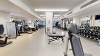 Located at 255 Warren St in Jersey City, NJ, this fitness center offers a generously sized, single-floor exercise facility designed to accommodate a full spectrum of workout needs. The space features a clean, modern aesthetic with crisp white walls, smooth light-toned flooring, and bright linear ceiling fixtures that provide consistent, even illumination throughout.

The cardio zone lines one side of the facility and is outfitted with a robust selection of machines, including treadmills, ellipticals, stationary bikes, and rowing equipment — offering users a wide variety of aerobic training options. On the opposing side, a dedicated strength training area houses cable machines, multi-use weight stations, and functional training equipment. A well-stocked free weights section includes an extensive rack of dumbbells paired with adjustable benches and wall-mounted mirrors, creating an ideal environment for resistance training.

A functional training zone rounds out the facility, featuring medicine balls, balance trainers, and suspension equipment, complemented by motivational athletic murals that energize the space. Large framed mirrors are positioned strategically throughout, enhancing the sense of openness. The climate-controlled environment, recessed lighting accents, and glass-panel entry doors contribute to the polished, professional atmosphere of this well-appointed fitness center.