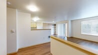 Located in Troutdale, Oregon, this two-bedroom, two-bathroom single-floor residence offers a functional and well-organized layout. The open-concept kitchen and living area forms the heart of the home, featuring light wood cabinetry, a peninsula counter, and white appliances including a refrigerator, stove, and microwave. Wood-look flooring flows throughout the main living areas, adding warmth and continuity to the space.

The living room is bright and airy, benefiting from a sliding glass door that opens to a private patio, flanked by a side window that further enhances natural light. Built-in open shelving along one wall provides practical storage and display space.

The primary bedroom is a comfortable size, finished with plush carpeting and a generous walk-in closet with built-in shelving and hanging rods. A second bedroom, also carpeted and naturally lit by a window with blinds, offers flexible use as a guest room or home office.

The two bathrooms differ in style: one is a full bath with a soaking tub/shower combo, wood-finish vanity, and wood-look flooring, while the second is a half bath featuring a pedestal sink, mirrored medicine cabinet, and overhead cabinetry. Together, the rooms offer a clean, neutral palette and practical living throughout.