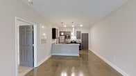The Keenan unit is a one-bedroom, one-bathroom residence spread across a single floor, offering an efficient and well-designed layout. The open-concept living and kitchen area serves as the heart of the space, anchored by polished concrete floors that lend an industrial yet refined character throughout.

The kitchen is a standout feature, equipped with stainless steel appliances including a refrigerator, microwave, and range. Dark espresso and gray cabinetry provide a bold contrast against white subway tile backsplash and light-toned countertops. A peninsula with seating overhang creates a natural division between the kitchen and living area, functioning as both a prep space and casual dining surface. Pendant lighting drops above the peninsula, complementing the recessed lighting throughout and enhancing the modern aesthetic.

White walls and clean baseboard trim keep the space feeling bright and cohesive, while the polished concrete floors add visual continuity from room to room. The layout is straightforward and functional, with clearly defined zones for living, cooking, and private sleeping quarters, making the most of the available footprint.