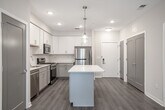 Located at 36 S New York Rd in Galloway, NJ, this single-floor unit presents a clean, modern aesthetic throughout its thoughtfully designed layout. The open-concept living and kitchen area serves as the heart of the space, where light wood-look flooring flows seamlessly underfoot and crisp white walls create a bright, airy atmosphere. Pendant lighting and flush-mount fixtures provide tasteful illumination across the space.

The kitchen is well-appointed with white shaker-style upper cabinets, contrasting gray lower cabinets, quartz countertops, and a full suite of stainless steel appliances including a gas range, over-the-range microwave, refrigerator, and dishwasher. A kitchen island adds additional counter space and a natural transition into the living area.

The living room opens directly to an outdoor deck through a sliding glass door, inviting natural light and outdoor views into the space. Multiple bedrooms feature the same light wood-look flooring and neutral warm-toned walls, offering versatile layouts.

Two bathrooms serve the unit, each finished with marble-look tile flooring. One bathroom features dark accent tile in the shower surround, while the other includes a tub-shower combination with accessible grab bars and a white vanity, providing both style and functionality.