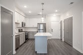 Located at 36 S New York Rd in Galloway, NJ, this single-floor unit presents a clean, modern aesthetic throughout its thoughtfully designed layout. The open-concept living and kitchen area serves as the heart of the space, where light wood-look flooring flows seamlessly underfoot and crisp white walls create a bright, airy atmosphere. Pendant lighting and flush-mount fixtures provide tasteful illumination across the space.

The kitchen is well-appointed with white shaker-style upper cabinets, contrasting gray lower cabinets, quartz countertops, and a full suite of stainless steel appliances including a gas range, over-the-range microwave, refrigerator, and dishwasher. A kitchen island adds additional counter space and a natural transition into the living area.

The living room opens directly to an outdoor deck through a sliding glass door, inviting natural light and outdoor views into the space. Multiple bedrooms feature the same light wood-look flooring and neutral warm-toned walls, offering versatile layouts.

Two bathrooms serve the unit, each finished with marble-look tile flooring. One bathroom features dark accent tile in the shower surround, while the other includes a tub-shower combination with accessible grab bars and a white vanity, providing both style and functionality.