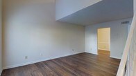 This two-floor space is designed with a clean, minimalist aesthetic that emphasizes openness and functionality. The main living area immediately stands out with its dramatically high ceilings, which create an expansive, airy atmosphere and lend the space a sense of grandeur. A partial upper-level overhang adds architectural interest and visual depth to the room, giving it a distinctive, multi-dimensional character.

Rich, dark hardwood flooring runs throughout the main level, providing a warm contrast to the crisp, neutral-toned walls painted in soft shades of white and light gray. The combination of these elements results in a cohesive and timeless interior palette that suits a variety of furnishing styles.

The open layout of the main living area flows naturally into an adjacent room, hinting at a well-connected floor plan that encourages ease of movement between spaces. White baseboards and trim throughout add a polished, finished look to each room.

The second floor contributes additional functional living space, making this property well-suited for those seeking defined areas for different activities. Overall, the space balances architectural distinction with practical design, offering a bright, neutral canvas ready to accommodate a range of uses and personal styles.