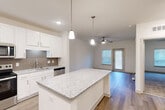 This well-appointed 1-bedroom, 1-bathroom unit in Dalton, GA offers a thoughtfully designed open-concept layout that maximizes every square foot. The kitchen serves as a central highlight, featuring crisp white shaker cabinetry, granite countertops, a tile backsplash, and a full suite of stainless steel appliances including a French door refrigerator, electric range, microwave, and dishwasher. A central kitchen island with pendant lighting above provides additional prep space and a natural transition into the living area. The living room is bright and airy, with wood-look plank flooring, a ceiling fan, and a door leading to a window-lit exterior access point. The bedroom offers plush carpeting, a ceiling fan, a natural light window, and direct access to both a dedicated closet and the bathroom. The bathroom includes a soaking tub with tiled surround and wood-look flooring. Additional spaces include a utility room and hallway, rounding out a functional floor plan. Recessed lighting and pendant fixtures throughout contribute to a clean, modern aesthetic suited for comfortable everyday living.
