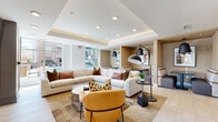 Located in the heart of uptown Charlotte at 425 W Trade St, this single-floor amenity space is designed to offer residents a refined and versatile communal environment. The lounge area is anchored by a generously sized sectional sofa and complementary seating in warm neutral tones, accented with rust and gold throw pillows. A tray ceiling with recessed and cove lighting adds architectural depth, while large floor-to-ceiling windows flood the space with natural light and frame views of the surrounding cityscape and outdoor pool area. A sleek linear fireplace and wall-mounted television enhance the lounge's comfort and functionality.

Adjacent to the lounge is a well-appointed kitchen and entertaining bar, featuring charcoal cabinetry with frosted glass inserts, a textured mosaic tile backsplash, stainless steel appliances, and a large center island with a light wood base and crisp white countertop. A bold sputnik-style brass chandelier illuminates a long communal dining table surrounded by upholstered chairs, creating an ideal setting for group gatherings.

A bright game nook with large windows, light tile flooring, and high-top seating rounds out the space, offering a casual retreat with city views. Throughout, the design blends contemporary style with warm, inviting materials.