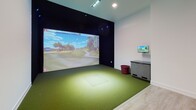 Located at 12501 Ridgedale Drive in Minnetonka, Minnesota, this single-floor indoor golf simulator suite offers a well-appointed space designed for both play and relaxation. The layout is divided into two distinct yet connected areas: a dedicated golf simulator bay and a comfortable lounge seating area.

The simulator bay is the centerpiece of the space, featuring a large projection screen that displays highly detailed, photorealistic golf course visuals. The hitting area is finished with artificial turf, providing an authentic feel underfoot, while dark acoustic wall panels and ambient blue accent lighting create an immersive, focused atmosphere. A side console and monitor provide easy access to simulator controls and course selection.

Adjacent to the simulator bay, the lounge area offers a welcoming retreat for players and spectators alike. Light hardwood-style flooring contrasts with a bold navy blue accent wall, giving the room a modern and energetic character. Colorful striped armchairs and ottomans are arranged around a central coffee table, creating a social gathering space. A wall-mounted flat-screen TV keeps guests engaged between rounds. Recessed ceiling lighting throughout ensures the space is well-lit and inviting. Together, these two zones create a cohesive entertainment environment ideal for golf enthusiasts of all skill levels.