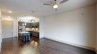 Located in Dallas, this single-floor residence offers a thoughtfully designed open-concept layout that seamlessly connects the living and kitchen areas. Rich, dark hardwood flooring runs throughout, anchoring the space with warmth and visual depth, while bright white walls and clean white baseboards create a crisp, modern contrast.

The living area is generously proportioned and illuminated by a sleek ceiling fan with an integrated light fixture, providing both comfort and style. The space flows naturally into the kitchen, which serves as a functional centerpiece of the home. The kitchen features dark gray flat-front cabinetry, light stone countertops with subtle veining, and a full suite of stainless steel appliances including a refrigerator, range, and microwave. A textured tile backsplash adds visual interest, while pendant lighting suspended above the kitchen island introduces an elegant, layered lighting scheme. The island itself offers additional prep and seating space, enhancing the kitchen's practicality.

The open design promotes an airy, connected atmosphere, making the space well-suited for both everyday living and entertaining. Overall, the interior carries a clean, contemporary aesthetic with high-quality finishes throughout.