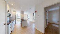 Located at 1 India St in Boston's vibrant waterfront district, this two-bedroom, two-bathroom residence offers a well-designed single-floor layout with modern finishes throughout. Light wood-tone flooring runs continuously across the living spaces, creating a warm and cohesive aesthetic.

The open-concept kitchen and living area serves as the heart of the home. The kitchen features white shaker-style cabinetry, a subway tile backsplash, stainless steel appliances including a refrigerator, range, and microwave, and a peninsula with a dark quartz countertop — ideal for casual dining or meal prep. Multiple windows flood the combined living space with natural light and frame views of Boston's surrounding cityscape.

Both bedrooms are bright and well-proportioned, each outfitted with large black-framed windows that invite ample daylight and offer views of the neighboring urban architecture. The generously sized primary bedroom provides comfortable living space, while the second bedroom offers flexibility for guests or a home office.

The two bathrooms are cleanly finished with white subway tile surrounds in the tub/shower combinations, dark countertops, and mirrored medicine cabinets. A hallway connects the rooms efficiently, contributing to the home's practical flow. Recessed lighting throughout adds a polished, contemporary touch to this well-appointed Boston residence.